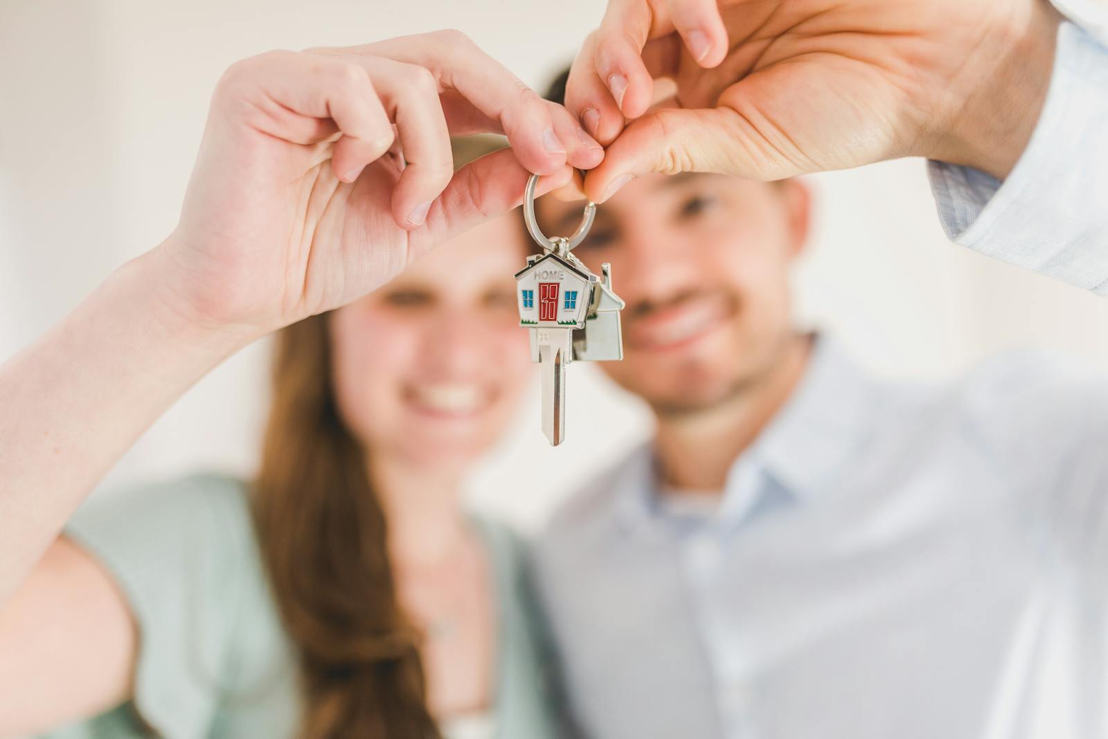Jeune couple souriant tenant la clé de leur premier logement, avec un porte-clés en forme de maison